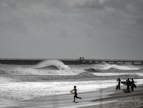 Large rough surf breaking near a pier on a cloudy beach