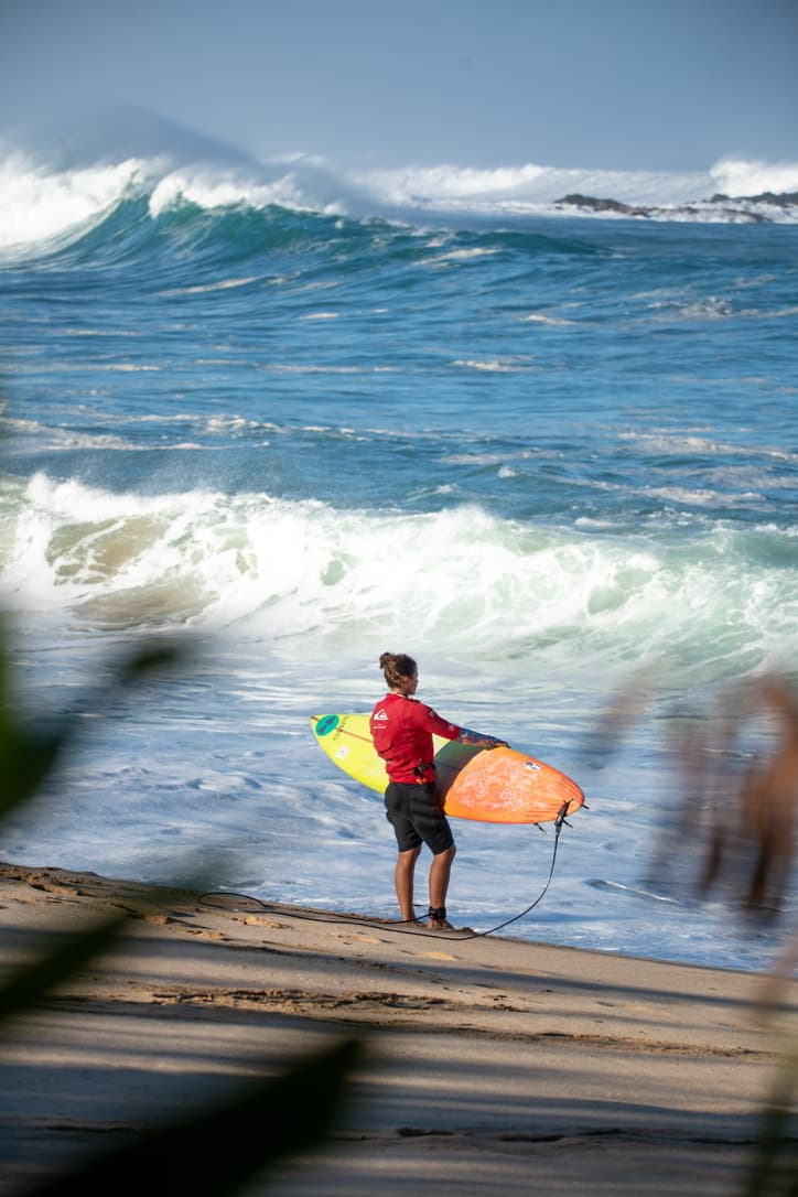 Surfer watching large blue waves from the beach with a bright surfboard