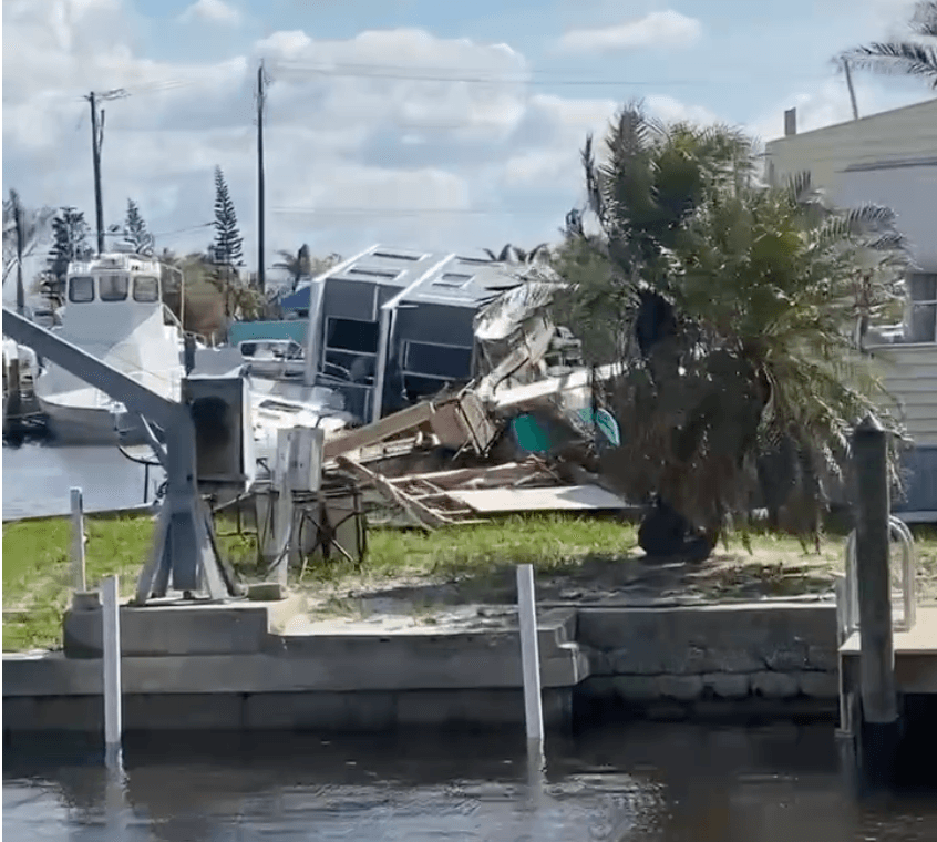 Damaged waterfront structure and palm trees beside a canal after storm surge