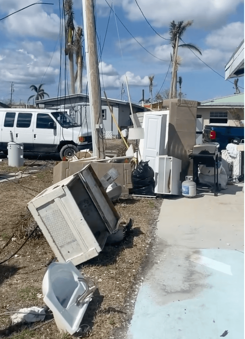 Storm debris, damaged utility lines, and household items beside a coastal home