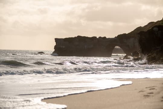 Ocean waves rolling toward a beach below a natural rock arch