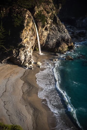 Small waterfall flowing onto a secluded beach beside clear blue water