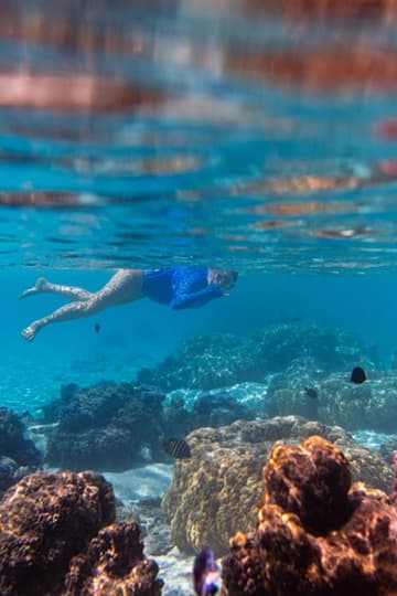 Swimmer moving above coral in clear blue water