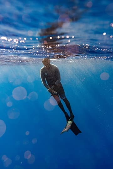 Freediver descending below the surface in blue water