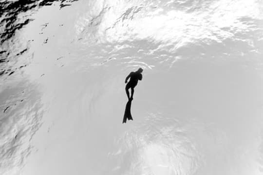Freediver seen in silhouette below the bright water surface