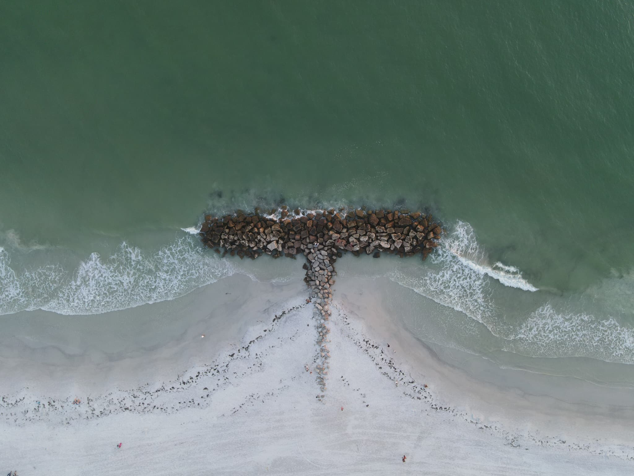 Overhead view of a breakwater cutting through green water near a sandy shoreline