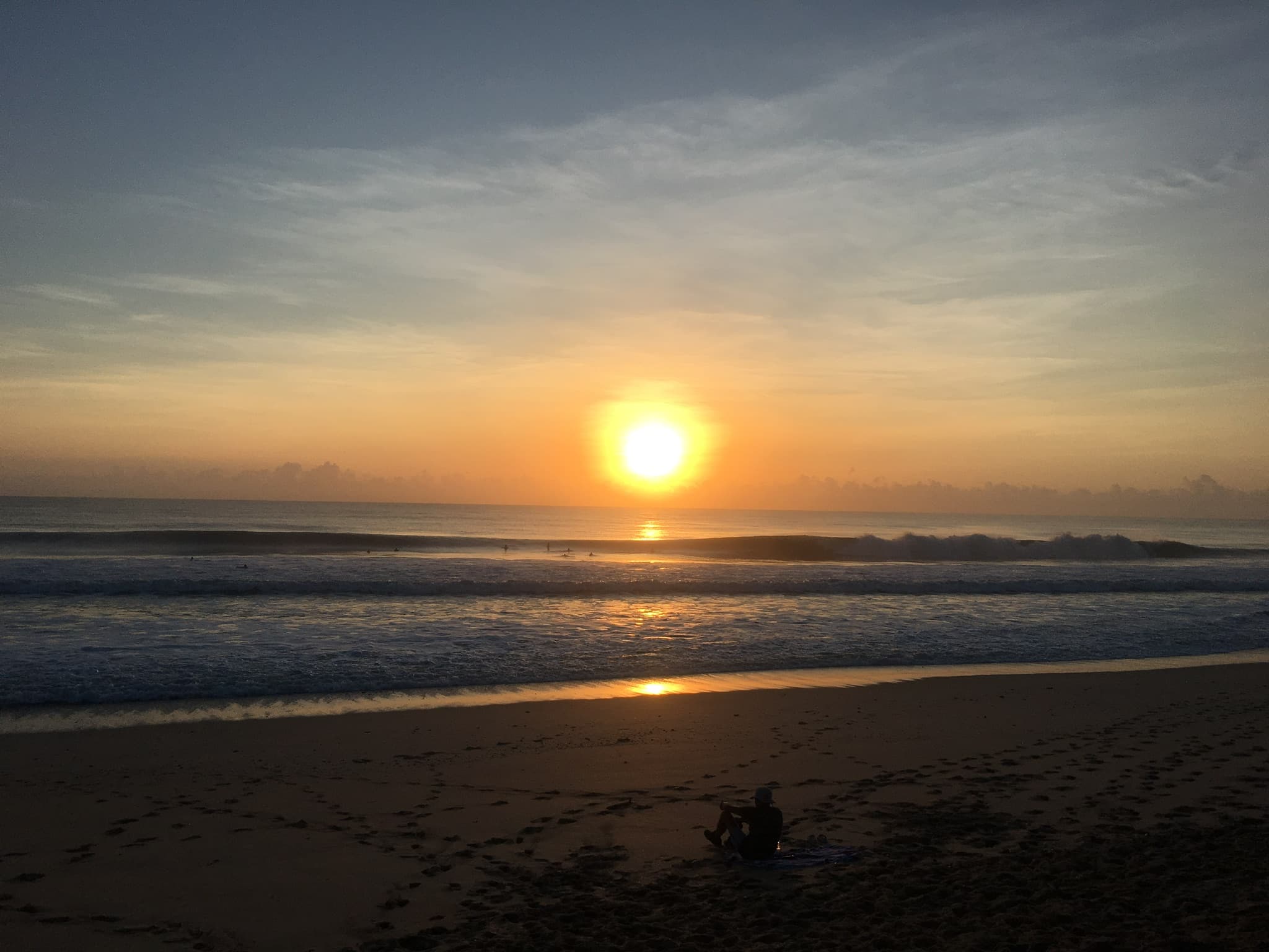 Sunrise surf rolling into a Florida beach with a person sitting on the sand