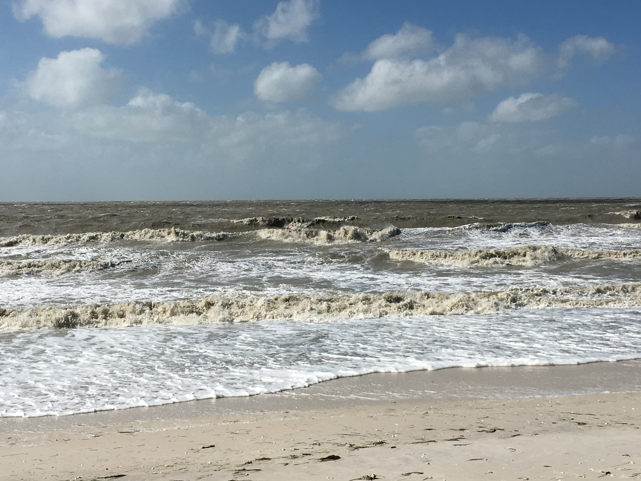 Rough surf breaking across a Florida beach under a blue sky