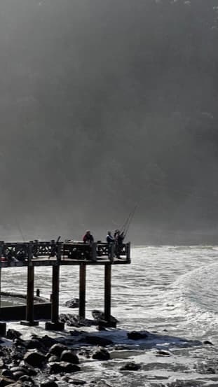 Anglers fishing from a pier in rough coastal water