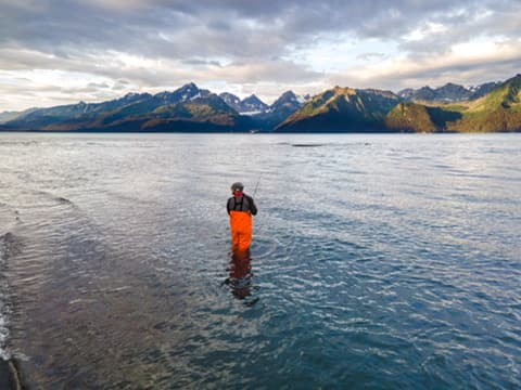 Angler wading in a broad mountain-lined bay