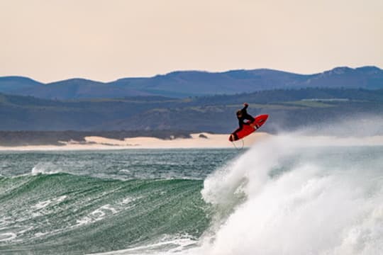 Surfer launching off a wave with a coastal mountain range behind the break