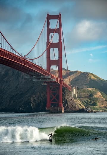 Surfer riding a wave below the Golden Gate Bridge
