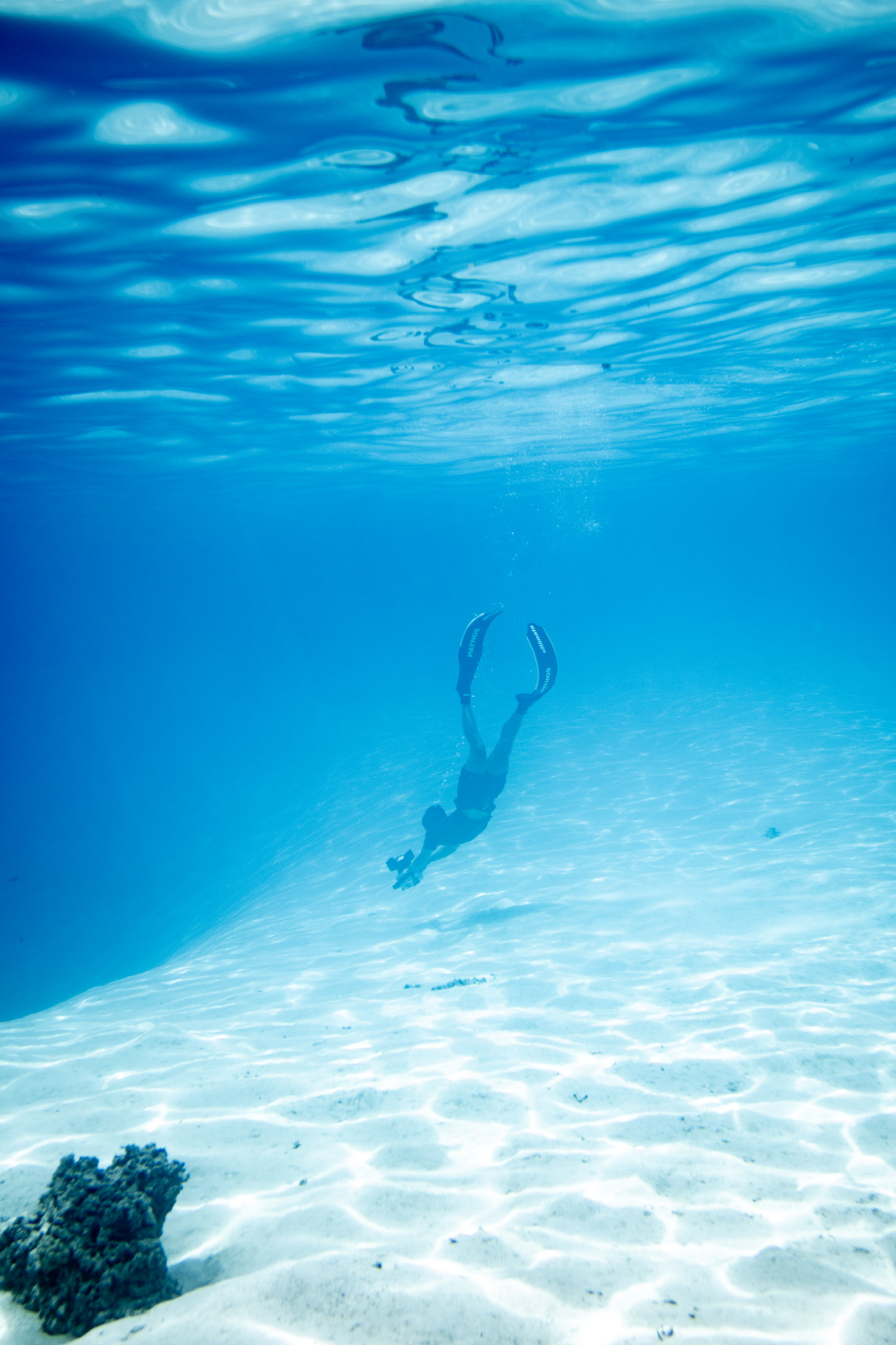 Diver swimming through clear blue water above a bright sandy bottom