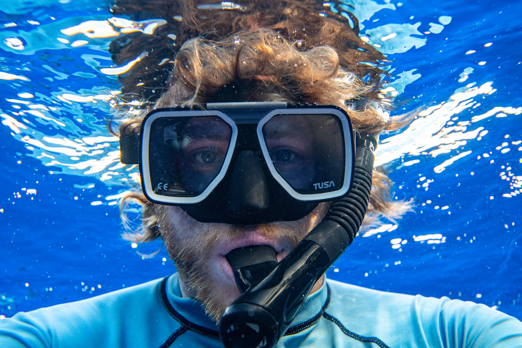 Close-up underwater view of a snorkeler wearing a mask in clear blue water